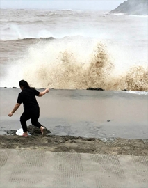 A woman walks along the seafront as strong waves break on shore ahead of the landfall of Typhoon Chan-Hom in Wenling in eastern China's Zhejiang province, on Friday, July 10, 2015. Chinese authorities have evacuated tens of thousands of people and canceled scores of trains as a super-typhoon with wind gusts up to 200 kilometers per hour (125 mph) heads toward the southeastern coast. (Chinatopix Via AP) CHINA OUT