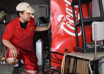 Free Topping Pizza owner Jason Rice looks at the Coca-Cola cooler, which he believes saved his life when a vehicle crashed through his storefront.