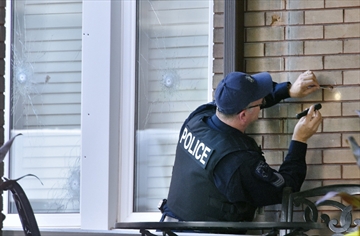 A Hamilton police officer collects bullets from the brick on the front of Pat Musitano's home on St. Clair Boulevard.